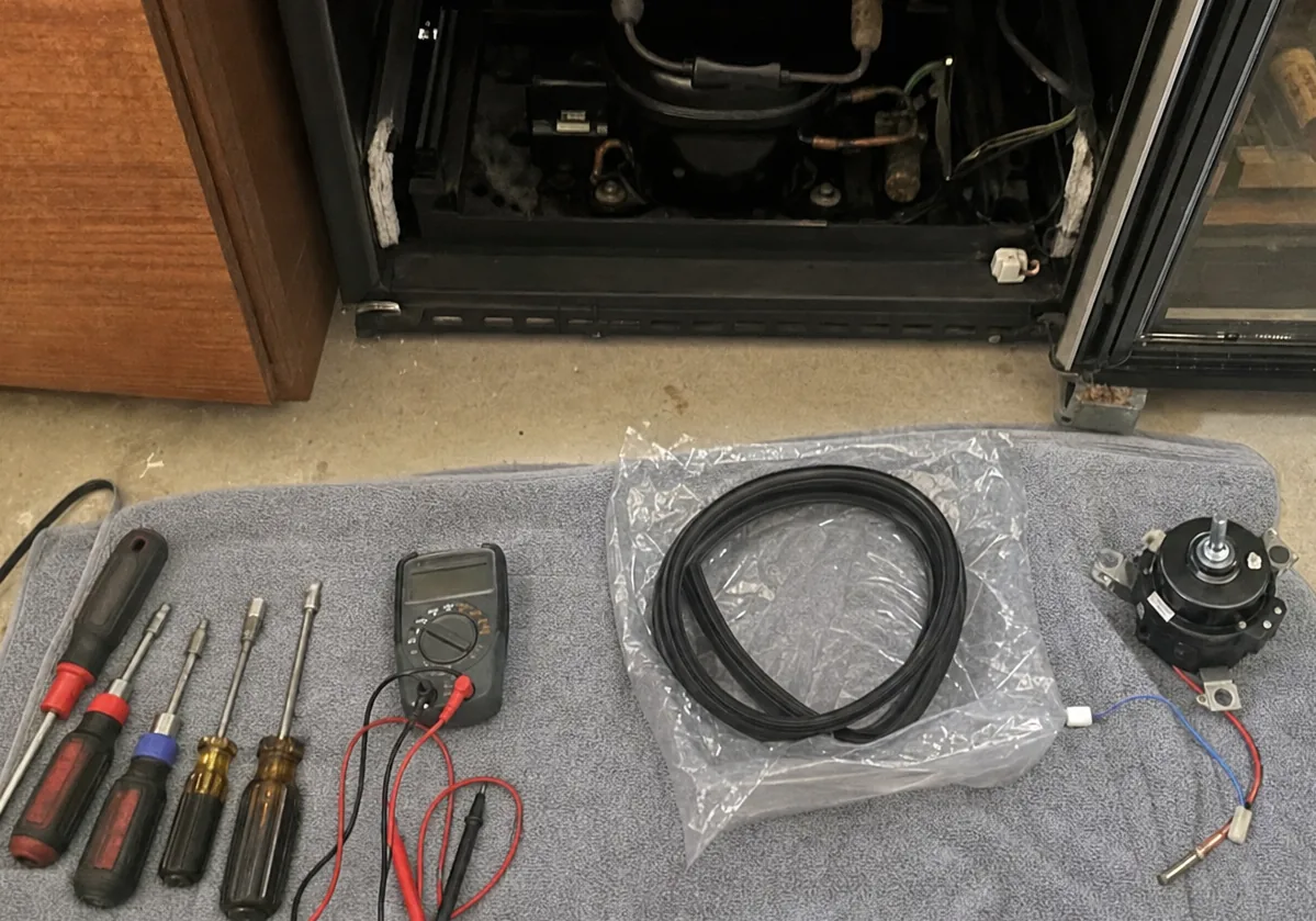 A close overhead view of a multimeter and a row of nut drivers laid in order on a towel, the leads coiled beside them and a sealed parts bag to one side.